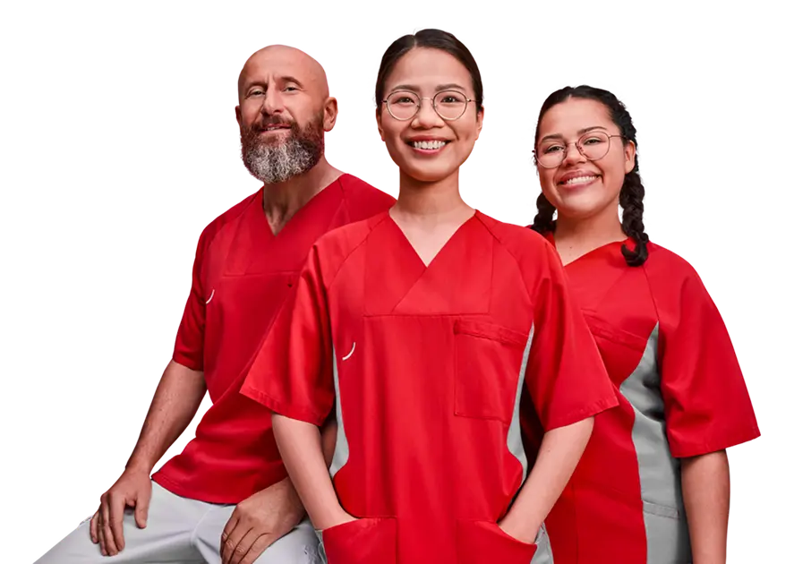Drei medizinische Fachkräfte in rot-grauer Berufskleidung stehen nebeneinander und lächeln in die Kamera. Eine Frau mit Brille steht im Vordergrund, ein bärtiger Mann links und eine weitere Frau mit Brille und geflochtenem Zopf rechts im Hintergrund.